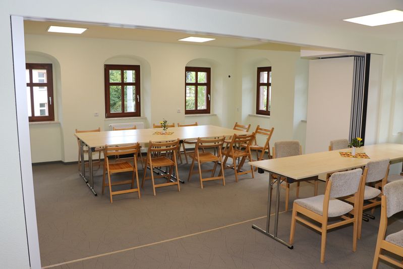 Heller Kantoratsraum mit grauen Teppichböden, mehreren Tischen, Holzstühlen und vier Fenstern mit Rundbögen. (Link öffnet Popup-Fenster mit vergrößertem Bild)