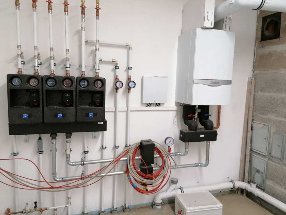 Eine moderne Gas-Brennwerttherme mit Pumpengruppen und komplexer Rohrleitungsinstallation an einer Wand.  (Link öffnet das Foto vergrößert in einem Popupfenster)